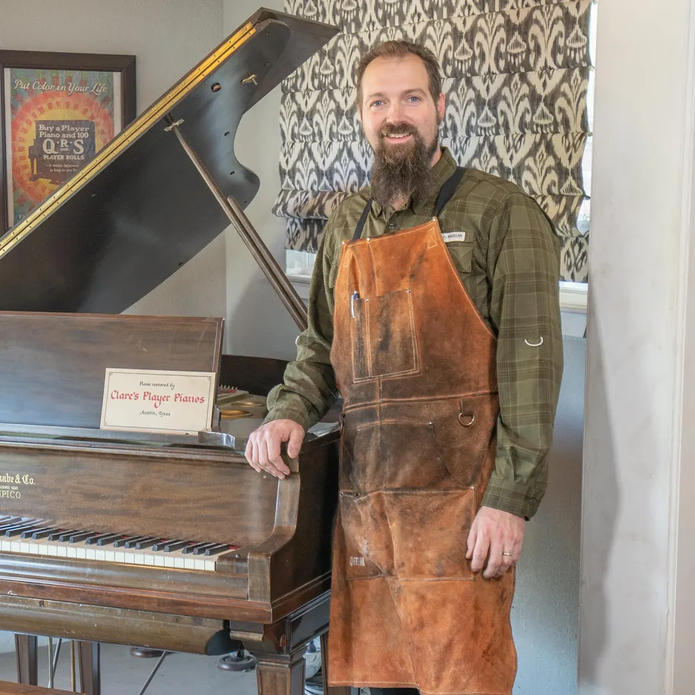 Justin Clare, third-generation piano technician, beside a restored grand piano